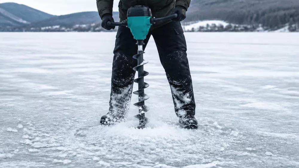 Electric ice auger drilling through ice on a frozen lake